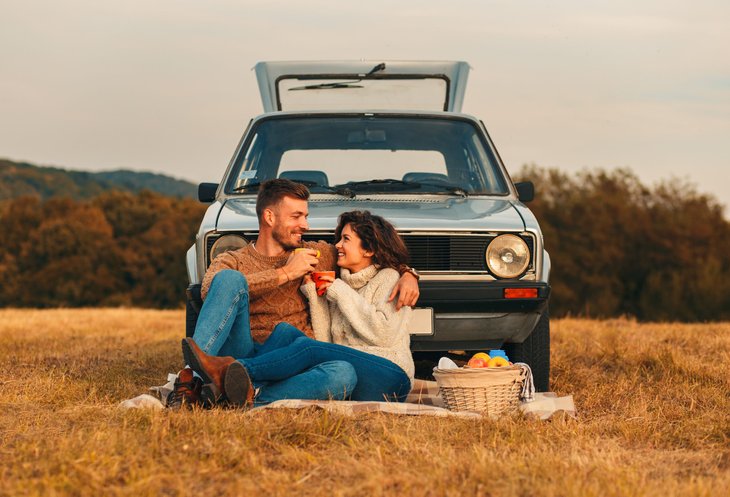 Couple having a picnic in front of an old car